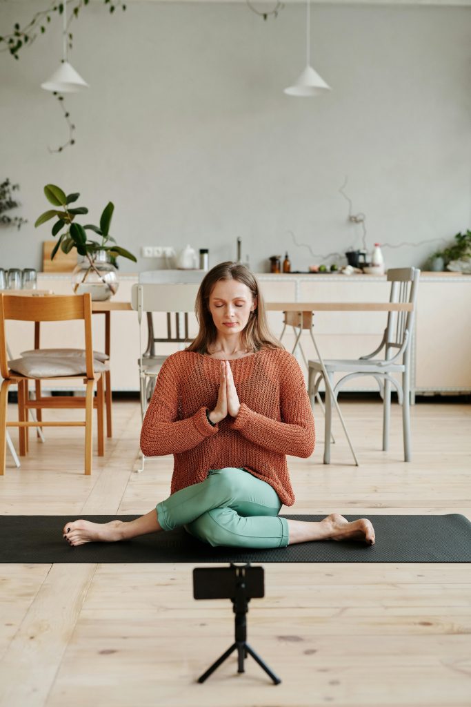 Woman practicing yoga on a mat indoors, with smartphone setup for video.